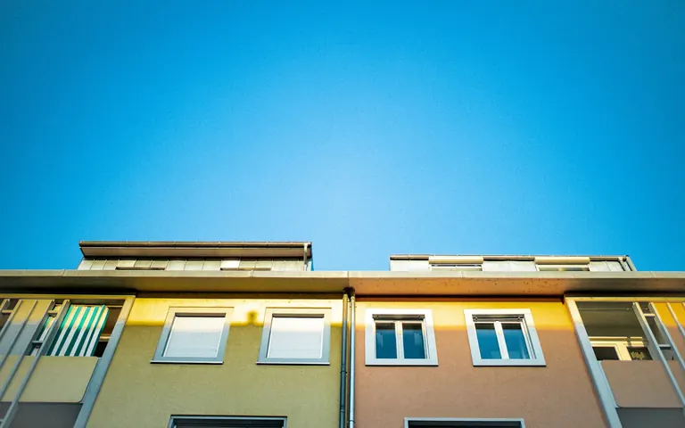 Helle Wohnhäuser im Grünen unter blauem Himmel